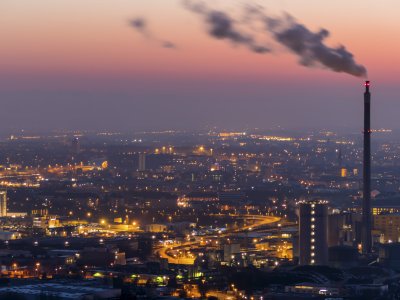 Smoke emits from a smokestack with a city skyline at sunset