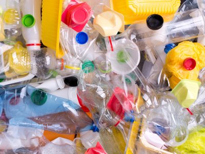 A large pile of colorful, crumpled plastic waste, including bottles, caps, food containers, and plastic bags, representing various types of disposable consumer plastics.